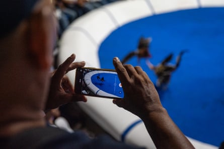 A person’s hands holds a cellphone aimed at a blue half circle with figures inside it