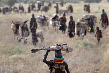 A group of people walk leading animals across scrubland.