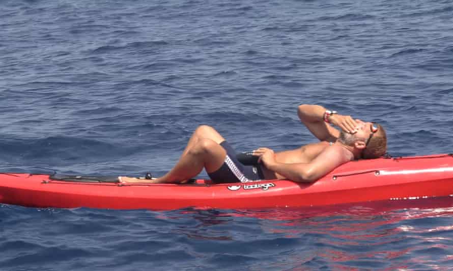 Ben lying on his back on a red support raft in the sea, one hand over his face