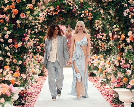 Woman in blue suit and woman in blue dress walk hand in hand under flower arches