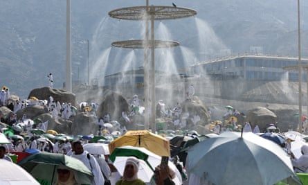 Mist is sprayed on to a crowd of people, many of whom are carrying umbrellas
