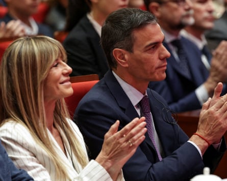 Begoña Gómez and Pedro Sánchez sitting next to each other in an auditorium applauding