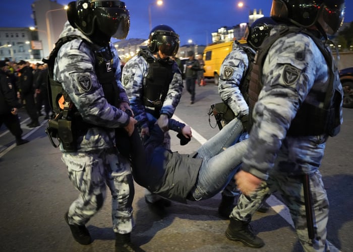 Man being carried by four police officers in riot gear