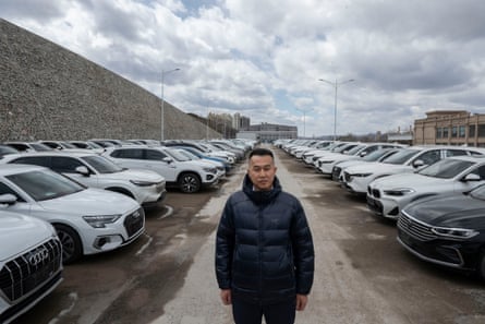 Gao Bin stands in the space between rows of cars parked at either side of him