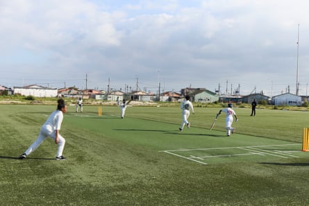 A wide view of a cricket match between two teams of African children on a ground in a township in Cape Town.