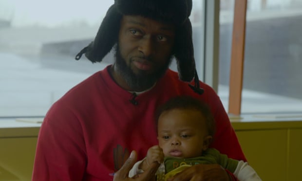 A man in a red shirt and winter hat with earflaps holds an infant boy.