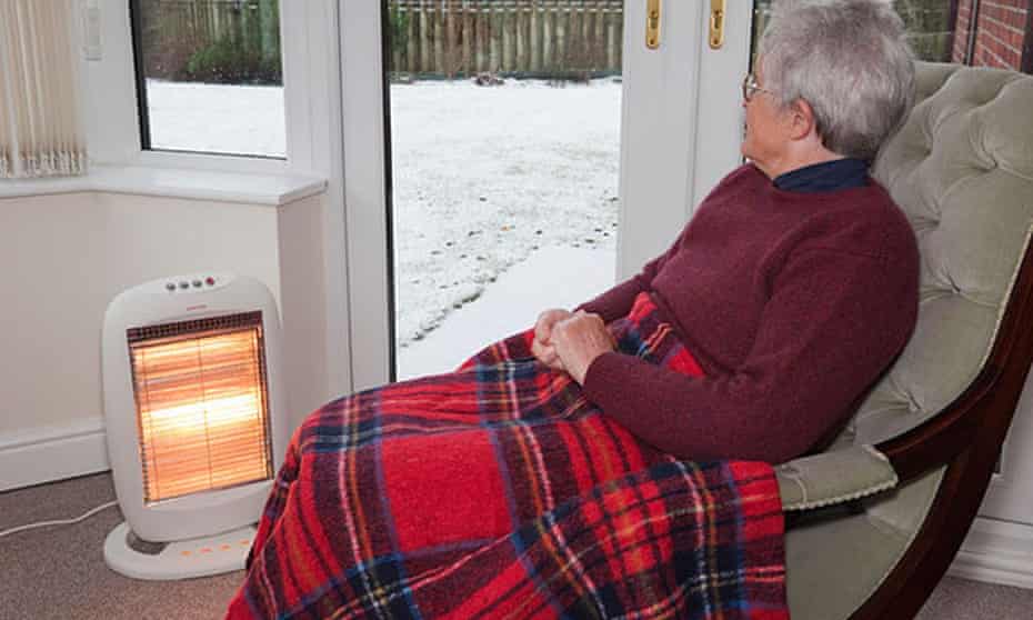 Older woman in rocker with rug on knees in front of heater with snow outside