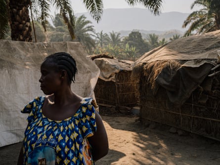 A black woman stands among palm huts.