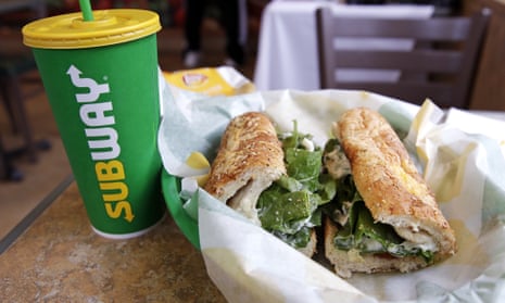 The Subway logo is seen on a soft drink cup next to a sandwich
