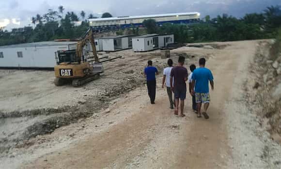 A group of refugees and asylum seekers walk by a construction site at the East Lorengau centre on Manus Island.
