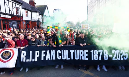 Fans marching through green flare smoke behind a banner that reads ‘RIP fan culture 1878-2025’