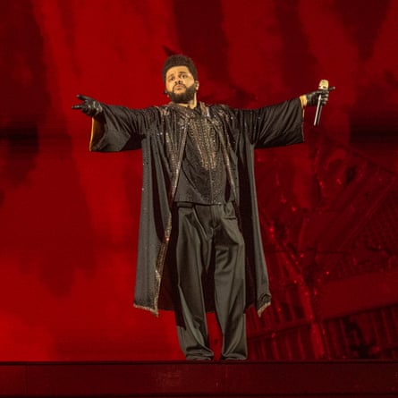 The Weeknd standing on stage in flowing black clothing with his arms outstretched