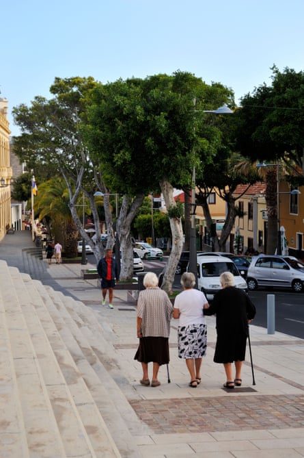 Three elderly women walk down a street, arm in arm