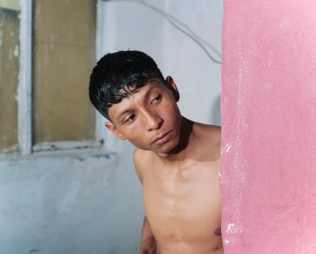 Shirtless boy peering around a pink wall.