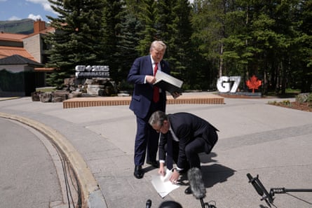 Starmer bent down picking up papers from the floor while Trump looks down