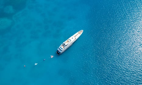 A superyacht seen from directly above in a vivid blue sea, with smaller watercraft around it