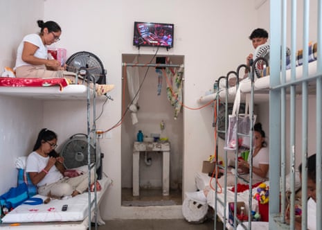 Women sitting on bunk beds sew and embroider in a shared cell