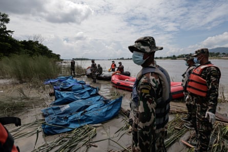 Soldiers stand over body bags of flood victims retrieved from a river