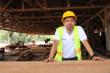 A man in a white shirt and yellow hard hat in a sawmill.