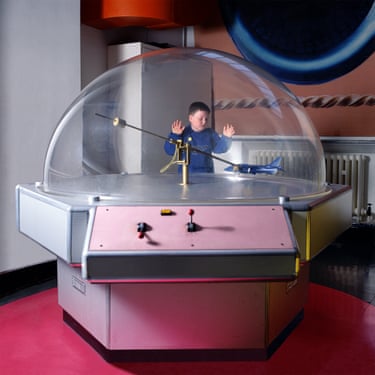 A boy in a blue sweatshirt places his hands on the outside of a glass ‘bubble’ within which is a small blue aircraft