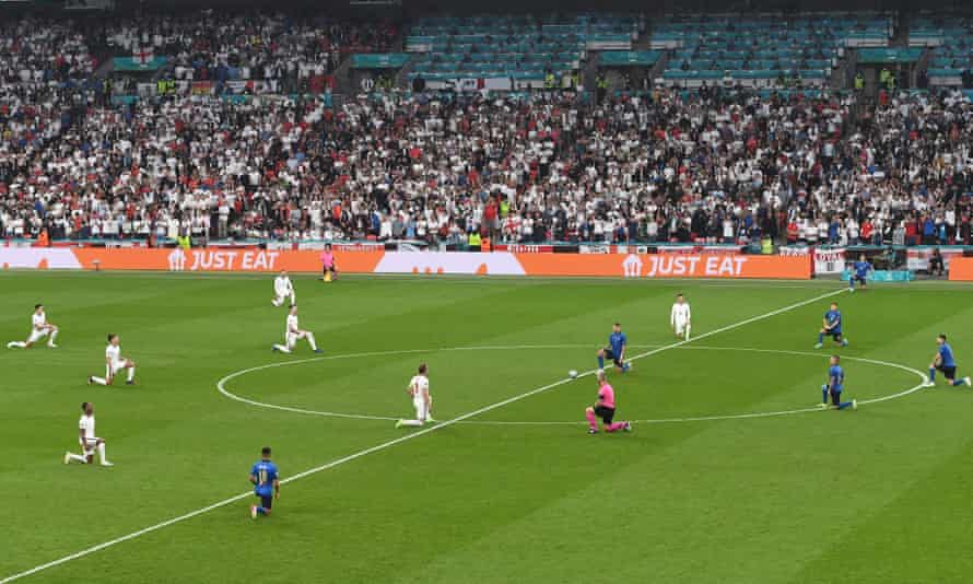 Wide shot of English players, in white, and Italian players, in blue, on one knee around center circle