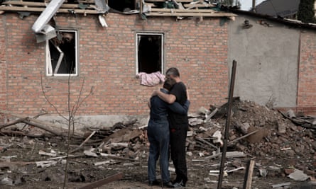 Damaged building with empty windows, rubble and two people consoling each other