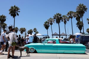 An aqua coloured car is parked on a road, with palm trees and blue sky behind