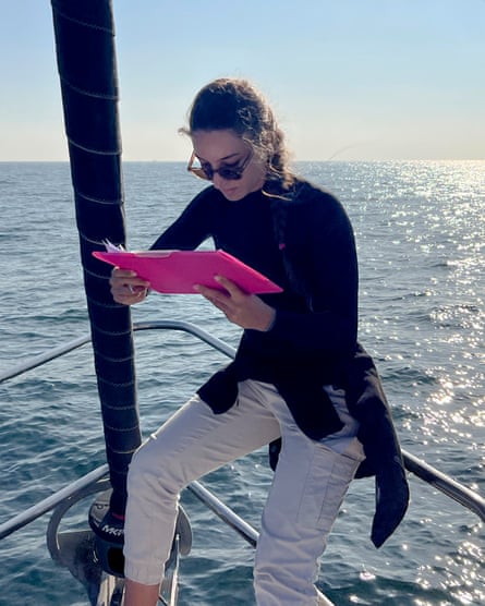 A young woman on the bow of a boat at sea looking at a folder