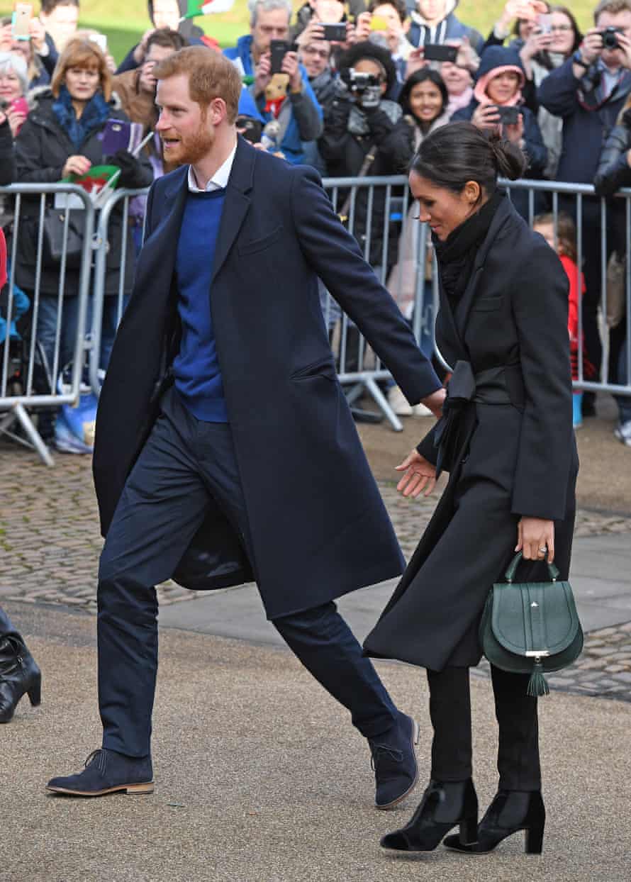 Meghan Markle with Prince Harry, wearing a Stella McCartney coat, Hiut jeans and a DeMellier London handbag