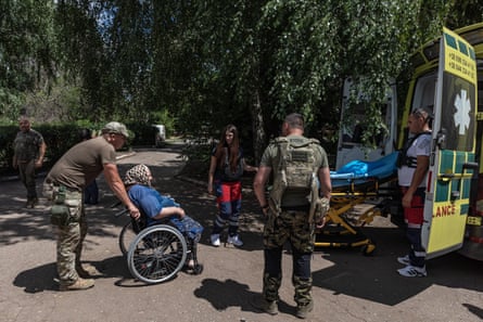 A woman in a wheelchair is helped into an ambulance by police.