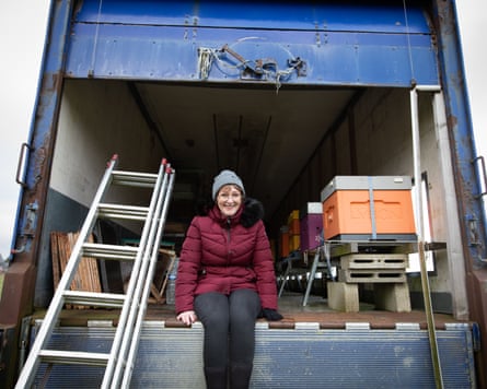 A woman sitting in the back of a van, which is filled with bee hives.