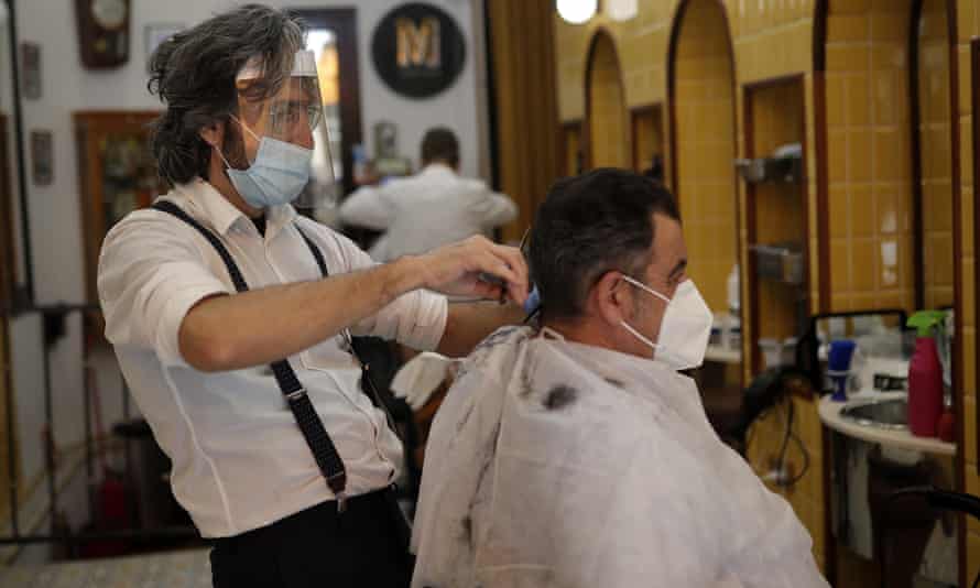 A barber cuts hair of a customer after small shops and businesses were allowed to reopen on Monday in Madrid