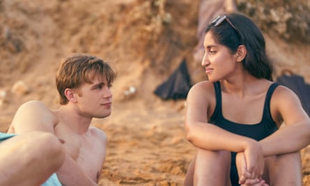 Leo Woodall and Ambika Mod as Dexter and Emma in One Day. They are on a beach, Woodall lying on his side looking at Mod.
