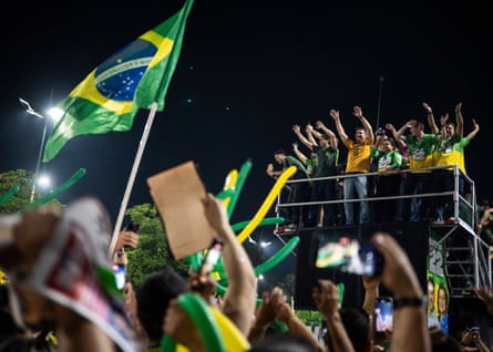 Flávio Bolsonaro waves to supporters from on top of a piece of scaffolding at a campaign rally