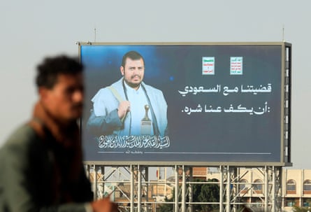Man walks past a massive billboard with a photo of Abdul-Malik al-Houthi on it