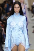 Model Bella Hadid, with long straight hair, wears a creased satin shirt with two lace discs on her chest