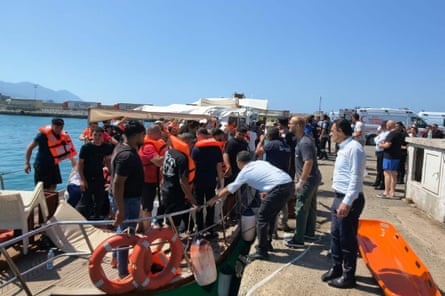 People wearing orange lifejackets get off a small boat on a quayside.