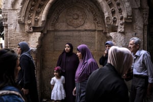 A woman and a young child stand in an ornate doorway as others walk past