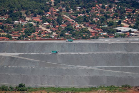 Mine tailings with two blue trucks driving next to residential buildings