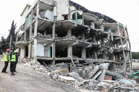 आपातकालीन कर्मचारी एक खंडहर इमारत के पास खड़े हैं