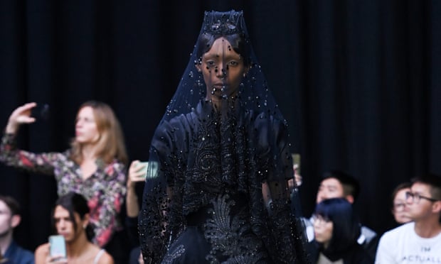 A model on the runway in a black dress and veil with a tiara