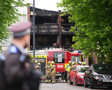 A fire enging and firefighters outside a burnt-out house with a police officer in the foreground
