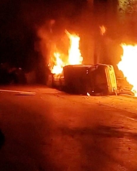 Still from a video shows fires burning and an overturned car