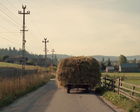A loaded hay cart drives away on a sunny rural road