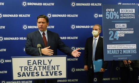 The Florida governor Ron DeSantis, left, stands in front of a sign reading "Early treatment saves lives". At right is Shane Strum, CEO of Broward Health