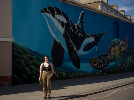 A woman stands in front of a large mural depicting a whale and turtle