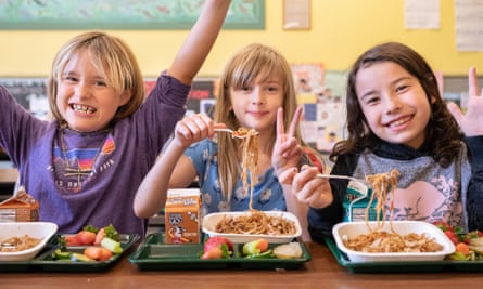 Three kids eating yakisoba noodle school lunches enthusiastically.