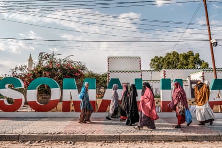 Women walk in front of tall letters that spell out Somaliland decorated in the pattern of the state’s flag.