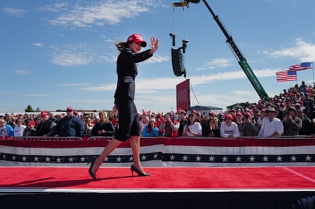 woman in a red baseball cap walks across a stage in front of lots of people