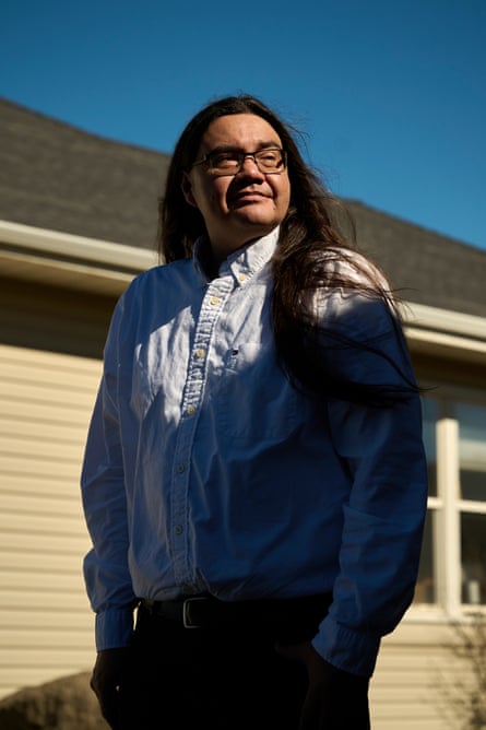 A man with long hair and wearing a white shirt poses with his face turned toward the sun.